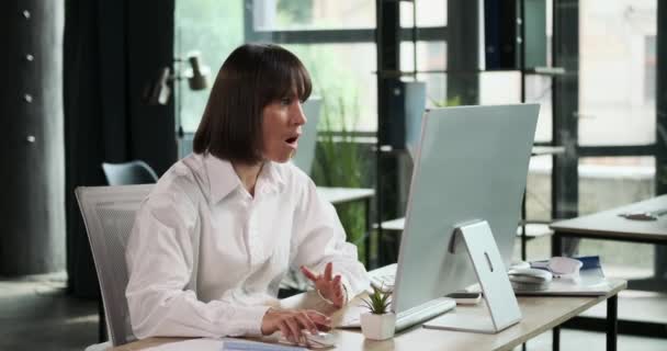 女性のオフィスワーカーは 彼女のコンピュータ画面上のニュースによって明らかに苦しめられています 彼女の怒ったブラウと厄介な表情は 情報に対する彼女の感情的な反応を明らかにします — ストック動画