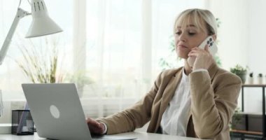 Keyifli Kafkasyalı iş kadını, hoş bir telefon görüşmesi yaparken kaygısız görünüyor ve laptopunu etkili bir şekilde kullanıyor. Neşeli bir gülümseme ve rahat bir tavırla.