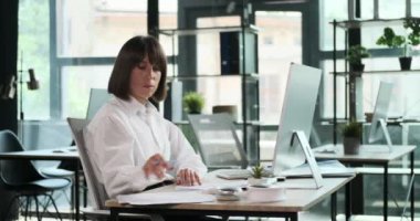 Kendini işine adamış bir kadın girişimci ofiste hem evrak işlerini hem de bilgisayar görevlerini yürütür. Belgeleri incelemekle bilgisayarı üzerinde çalışmak arasında kusursuz geçiş yaptığı için çok yönlü çalışma yetenekleri parlıyor..