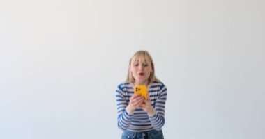 Tatmin olmuş ve neşeli bir kadın beyaz bir arka planda, elinde telefonla 