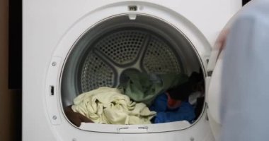 Verimlilik ve amaçla, bir kadın kurutucudan kuru ve sıcak giysiler alır. Hızlı hareketleri çamaşır yıkama sürecinin son adımını gösteriyor, kolaylık ve pratiği birleştirerek..