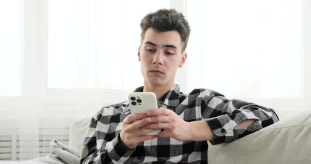 Sentado Sofá Hombre Parece Perdido Pensamiento Mientras Sostiene Teléfono Mirada — Vídeos de Stock