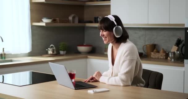 Biała Kobieta Nosząca Słuchawki Wykonuje Rozmowę Wideo Używając Laptopa Kuchni — Wideo stockowe