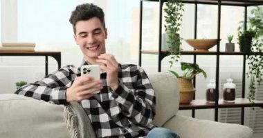 Oturma odasında, genç bir adam telefonunu kullanırken kahkahaya boğuldu. Sahne, onun gerçek neşesini ve eğlencesini yakalıyor, bir neşe ve pozitif enerji anı yaratıyor..