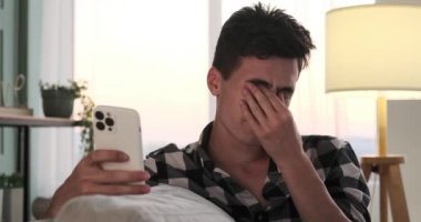 Kanepede, düşünceli beyaz bir adam telefonunu üzüntü belirtisiyle kullanır. Durgun atmosfer, onun düşünceli ruh halini yansıtıyor. Duygularının aralığını gösteriyor..