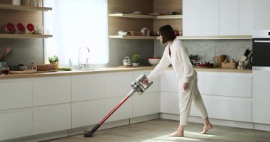 Beyaz bir kadın mutfağı temizlemek için elektrikli süpürge kullanıyor. Onun gayretli temizlik çabaları onun düzenli ve hijyenik bir yaşam alanını korumaya olan bağlılığını yansıtıyor..