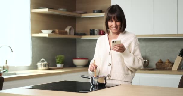 Radosna Kobieta Wielozadaniowa Posługująca Się Telefonem Umiejętnie Przygotowując Jedzenie Kuchence — Wideo stockowe