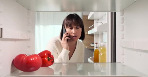 그녀의 전화를 사용하여 여성은 냉장고의 내용을 검사하고 식료품 주문을 진행합니다 — 비디오