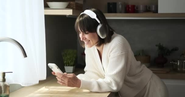 Gülümseyen Neşeli Beyaz Bir Kadın Mutfakta Telefonuyla Mesajlaşır Pozitif Havası — Stok video