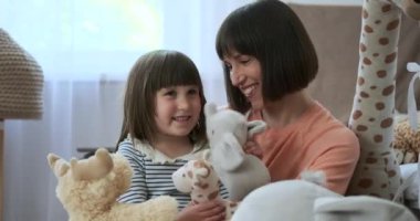 Çocuk odasında hoş bir sahnede, beyaz bir anne ve kızı yumuşak oyuncaklarla yaratıcı bir oyun oynuyorlar. Kahkahaları ve yaratıcılıkları odayı sıcaklıkla dolduruyor..