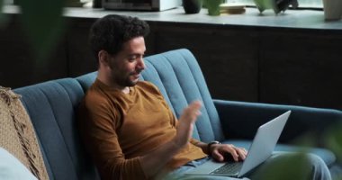 Neşeli bir adam, sıcak bir gülümseme ile, bir oturma odası kanepesinde rahatça otururken telefonla mesajlaşır. Olumlu tavrı ve rahatlığı modern iletişimin kolaylığını gösteriyor..