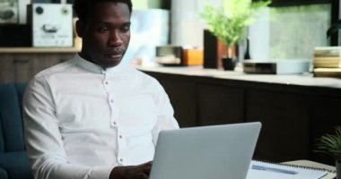 Ciddi bir Afro-Amerikan erkeği merkez ofiste dizüstü bilgisayarla çalışırken tamamen odaklanır. Görevlerine olan bağlılığı, kendini bu işe adamış verimliliğin bu sahnesinde açıkça görülüyor..