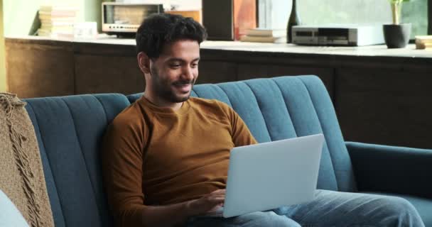 Homem Positivo Oriente Médio Senta Sofá Alegremente Digitando Seu Laptop — Vídeo de Stock