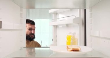 Akşamdan kalma beyaz bir adam buzdolabını açıyor ve bayat ekmek yemeyi tercih ediyor. Yemek seçimi, akşamdan kalma bir sabahtaki zorlukları yansıtıyor. Seçenekleri sınırlı olabilir..