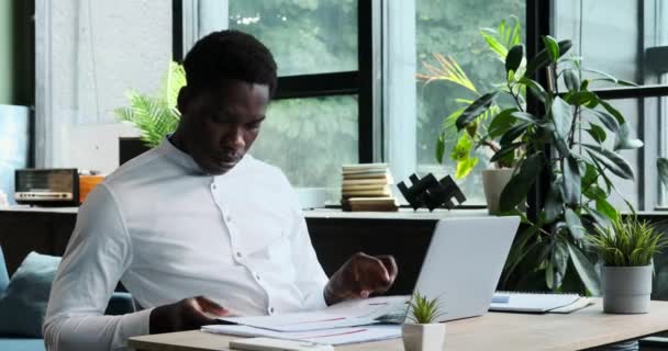 黒人のビジネスマンは 自宅のオフィスで机の上の書類を勤勉に整理しています 効率的なビジネス管理への彼のコミットメントは 焦点を絞った生産性のこのシーンで明らかです — ストック動画