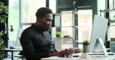 Sevinçli bir Siyahi girişimci bilgisayarın başında oturmuş başarı anını kutlarken yakalandı. Coşkusu ve neşesi aşikar, başarılarının zaferinin altını çiziyor..