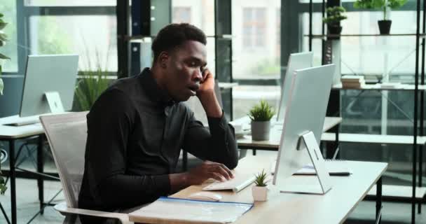 疲れた黒人ビジネスマンがオフィスのコンピューターに座り 明らかに仕事に疲れていた このシーンは プロの責任の課題と献身を反映しています — ストック動画