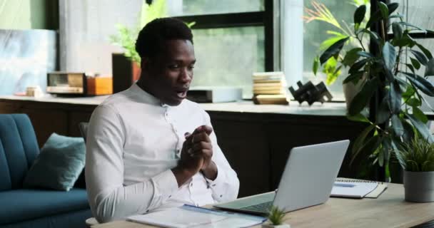 喜んでいるアフリカ系アメリカ人の男性は ホームオフィスで働いている間 成功の瞬間を祝っています 彼の喜びの表現と達成感は この達成のシーンで捉えられています — ストック動画
