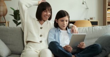 Gülümseyen anne ve oğul video görüşmesi için tablet bilgisayar kullanıyor. Işıl ışıl yüzleri ve etkileyici sohbetleri sıcaklık ve mutluluk iletir. Teknoloji aracılığıyla bağlı kalmanın verdiği hazzı gösterir..