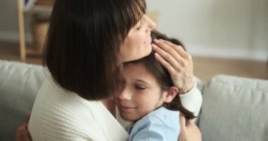 Sevgi dolu anne oğlunu oturma odasındaki kanepede sıcak bir şekilde kucaklıyor. Şefkatli jesti sevgi ve koruma taşıyor. Bu da onu anne bakımının ve aile yakınlığının iç açıcı bir sahnesi yapıyor..