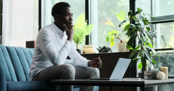 Задумчивый Черный Мужчина Сидит Диване Гостиной Глубоко Размышлениях Используя Ноутбук — стоковое видео