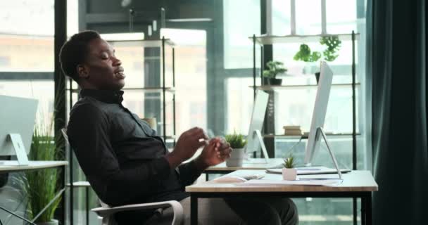 笑顔の黒人ビジネスマンがオフィスのデスクに座っています 彼の陽気な態度と肯定的な態度は プロの幸せと自信のこのシーンで明らかです — ストック動画