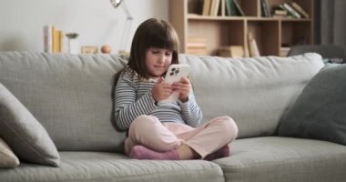 Kız oturma odasındaki kanepede oturuyor, telefonla meşgul. Cihaza olan masum merakı, günümüzün dijital çağındaki tipik genç çocukların merakını ve keşiflerini yansıtıyor..