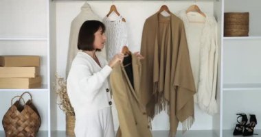 Beyaz kadın dolaba girer, dikkatlice seçer ve spor ceket dener. Odaklanmış ama düşünceli ifadesi moda karar verme sürecindeki ayrıntılara dikkat çekiyor..