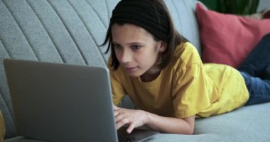 Huzurlu bir anda, konsantre olmuş bir okul çocuğu dizüstü bilgisayarına dalmış bir şekilde bir kanepede uzanır. Tereddüt etmeden yazarken parmakları klavyede dans ediyor..