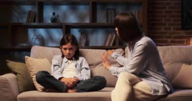 Anne, oğluna oturma odasında sert bir şekilde hitap ediyor. Sesi bir otorite ve endişe tonu taşıyor, odayı geriyor. Oğul, suçluluk ve meydan okuma karışımıyla dikkatle dinler..