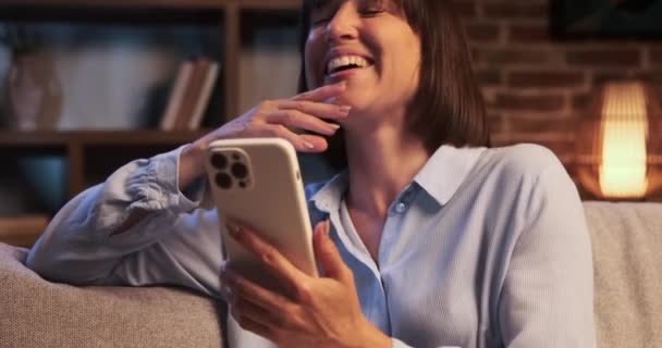 Woman Sits Sofa Phone Hand Bursts Laughter Room Filled Sound — Stock Video