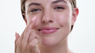Beyaz kadın yüz kremini nazikçe cildine yayıyor, parmakları nazikçe süzülüyor, armonik bir özen karışımı oluşturuyor ve temiz beyaz bir arka plana karşı kendini şımartıyor..