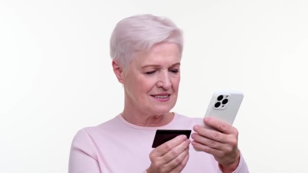 老年妇女自信地上网购物 手持电话和信用卡 她专注的表情和坚定的举止反映了她对购物的慎重考虑 — 图库视频影像