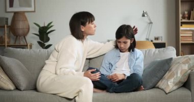 Anne, üzgün oğlunu oturma odasında kucaklarken derin bir şefkat gösteriyor. Onun rahatlatıcı jesti, zor bir zamanda empati ve sevgi gösteriyor..