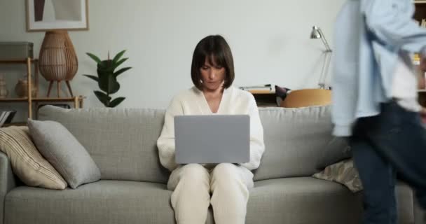 Mãe Focada Trabalha Diligentemente Laptop Enquanto Crianças Brincam Energeticamente Redor — Vídeo de Stock