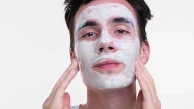 Mutlu adam bir krem maskeyle ortaya çıkıyor. Maske yumuşak, kremsi renk, beyaz arkaplanın saflığına karşı nazikçe zıtlaşır ve huzurlu bir görsel oluşturur..