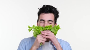 Beyaz adam marul yaprakları yemekten zevk alıyor. Gülümseme, dikkatle çiğnerken ışıl ışıl parlıyor. Salata arka planda kontrastı bırakır, doğallığı vurgular..