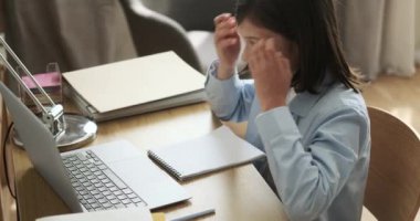 Çalışkan okul çocuğu masada oturur, dizüstü bilgisayar ve not defteriyle ödev üzerinde çalışır. Odaklanmış çabaları, okul ödevlerini tamamlama kararlılığını vurguluyor.