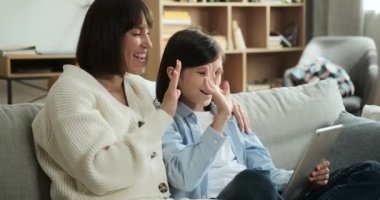 Anne ve oğlu video çağrısı için dijital tablet kullanıyor ve diğer taraftan birini selamlamak için coşkuyla el sallıyorlar. Onların neşeli etkileşimleri bir bağlantı ve iletişim duygusu ekler..
