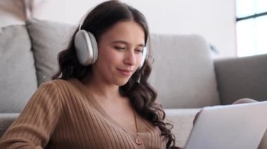 Oturma odasında kulaklık takan bir kadın portrede görüntülenir, dizüstü bilgisayara kaptırılır. Odanın ışıltısı sahneyi güzelleştirirken, odaklanmış ifadesi dijital görevlere olan bağlılığını ortaya koyuyor..