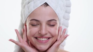 Kafasına havlu sarılmış bir kadın, temiz beyaz bir zemine karşı sakin bir ifadeyle yüzüne nazikçe dokunuyor. Zarif hareketleri ve odaklanmış tavrı bir anlık özgüvenini yansıtıyor..