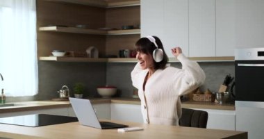 Kafkasyalı bir kadın mutfaktayken laptoptan keyifli haberler alıyor. Sevinçli ifadesi ve olumlu tepkisi mutluluk ve heyecan verici bilgileri iletiyor..