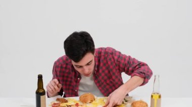 Açgözlü adam beyaz bir arka planda bir dilim pizzayı hevesle ısırıyor. Pizzanın peynirli ve lezzetli tadını çıkarırken gözleri beklenti ve zevkle parlıyor..