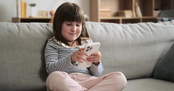Fröhliches Mädchen Sitzt Auf Der Wohnzimmercouch Und Hält Ihr Handy — Stockvideo