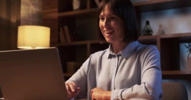 Kararlı bir kadın gece yarısı video konferans görüşmesi yapıyor. Yüzü ekranın yumuşak parıltısıyla aydınlanıyor. Odaklanma ve adanmışlık karışımı gösteriyor..