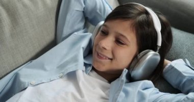 Kafkasyalı çocuk kanepeye uzanıp kulaklıkla müziğin tadını çıkarıyor. Onun rahat duruşu ve tatmin olmuş ifadesi sakin bir müzik değerini gösteriyor..