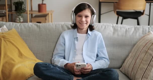 Boy Wearing Headphones Holding Phone Looks Directly Camera Warm Smile — Stock Video