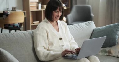Kafkasyalı kadın oturma odasındaki kanepede oturur dizüstü bilgisayar kullanır, işine dalmış, boş zamanlarında rahat ve rahat bir ortamda..