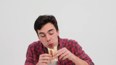 Fast food yemeğinin tadını çıkartan bir adam. Yüzü her lokmanın tadını çıkarırken hoş bir gülümsemeyle aydınlanır. Temiz beyaz bir arkaplan karşısında, o tatlardan zevk alır..