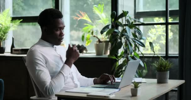思慮深い黒人の起業家は 自宅のオフィスで自分のラップトップにタイプするように深く考えています 彼の焦点と熟考のワークスタイルは 生産的な反射のこのシーンで明らかです — ストック動画